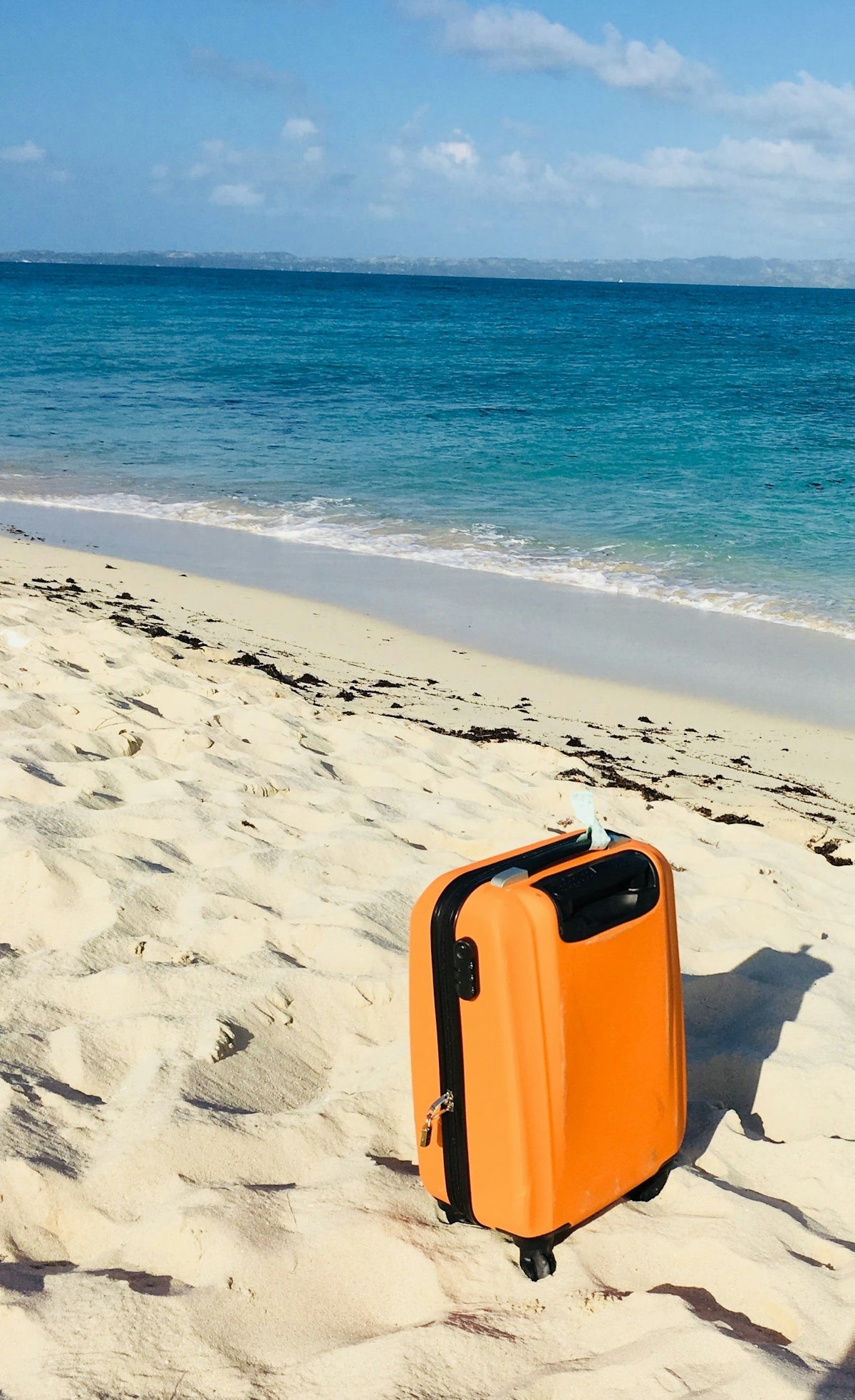 Oranger Reisekoffer allein an einem Sandstrand